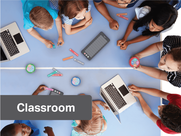8 children gather around a table with 2 laptops, 4 Vex 123 pucks, 3 vex 123 coding tablets, and a Vex 123 field 8 children gather around a table with 2 laptops, 4 Vex 123 pucks, 3 vex 123 coding tablets, and a Vex 123 field