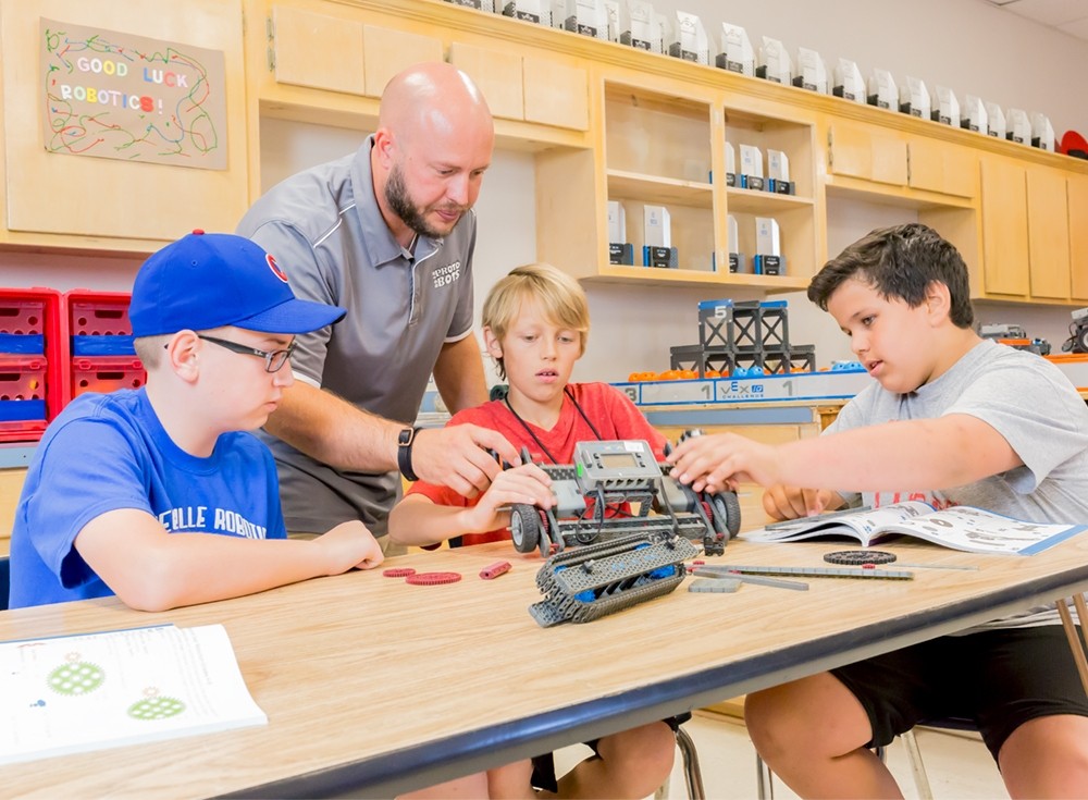 3 students working on a vex IQ robot are assisted by their teacher 3 students working on a vex IQ robot are assisted by their teacher